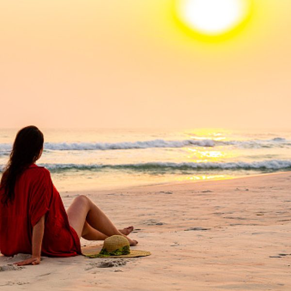 Woman sitting on sand with swimwear admiring sunset on the beach.